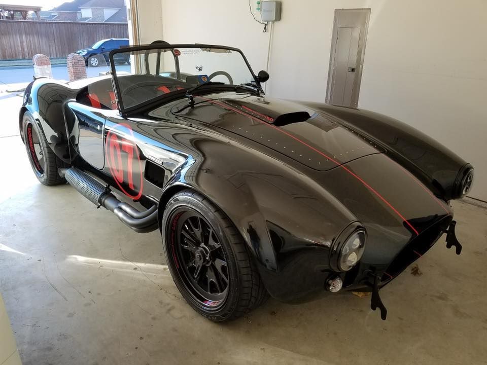 Black Shelby Cobra replica sports car in a garage with red accents.