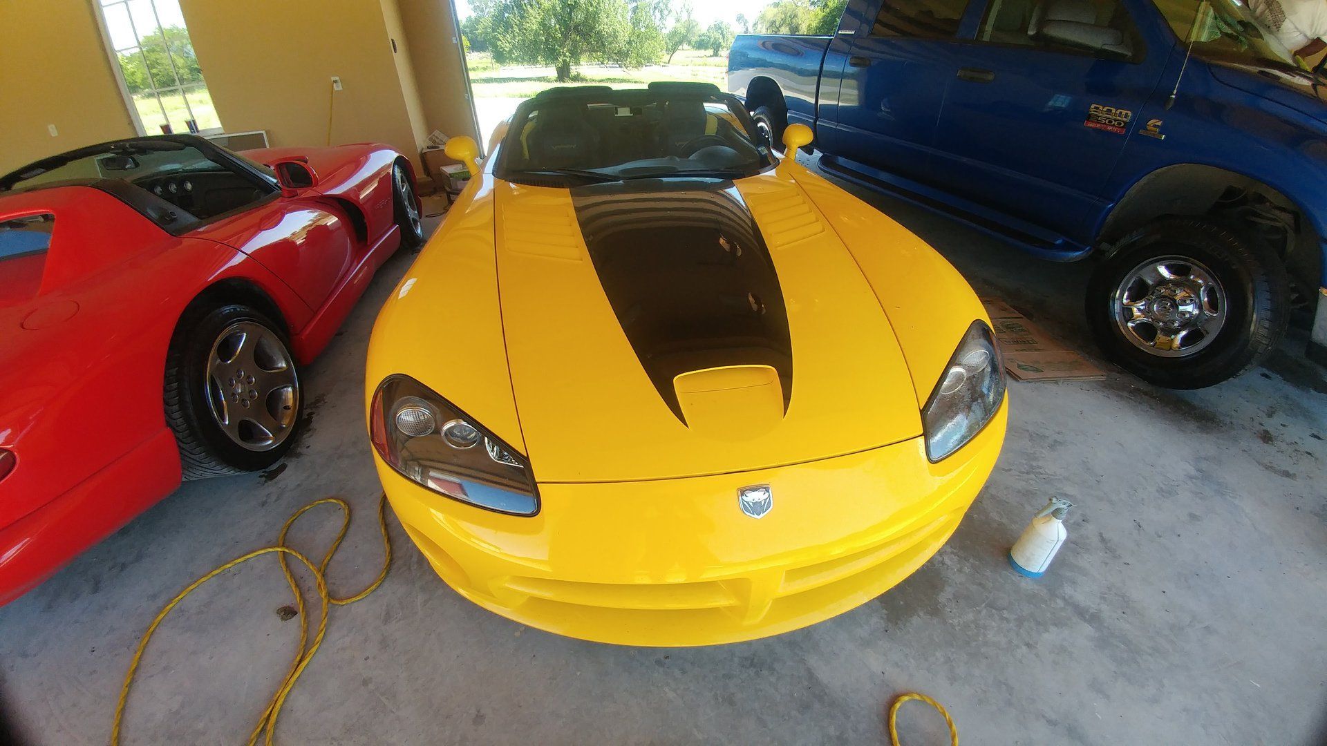 Yellow Dodge Viper with black stripe, parked next to a red car and a blue pickup truck.