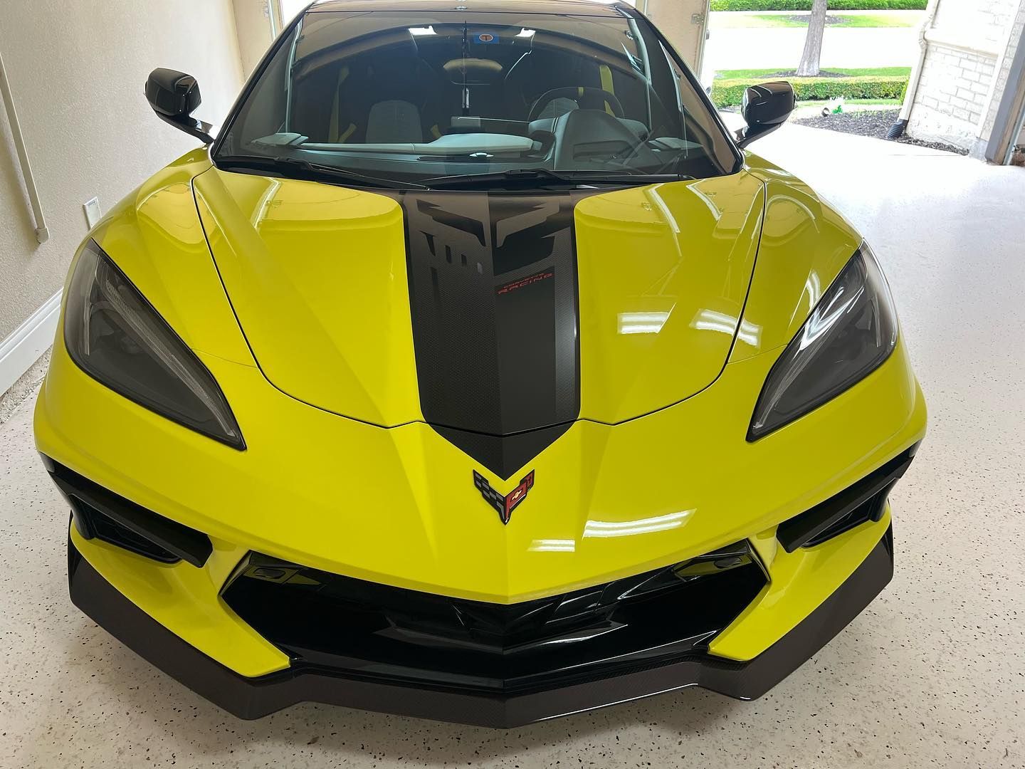 Yellow Chevrolet Corvette sports car with black racing stripe, parked indoors.