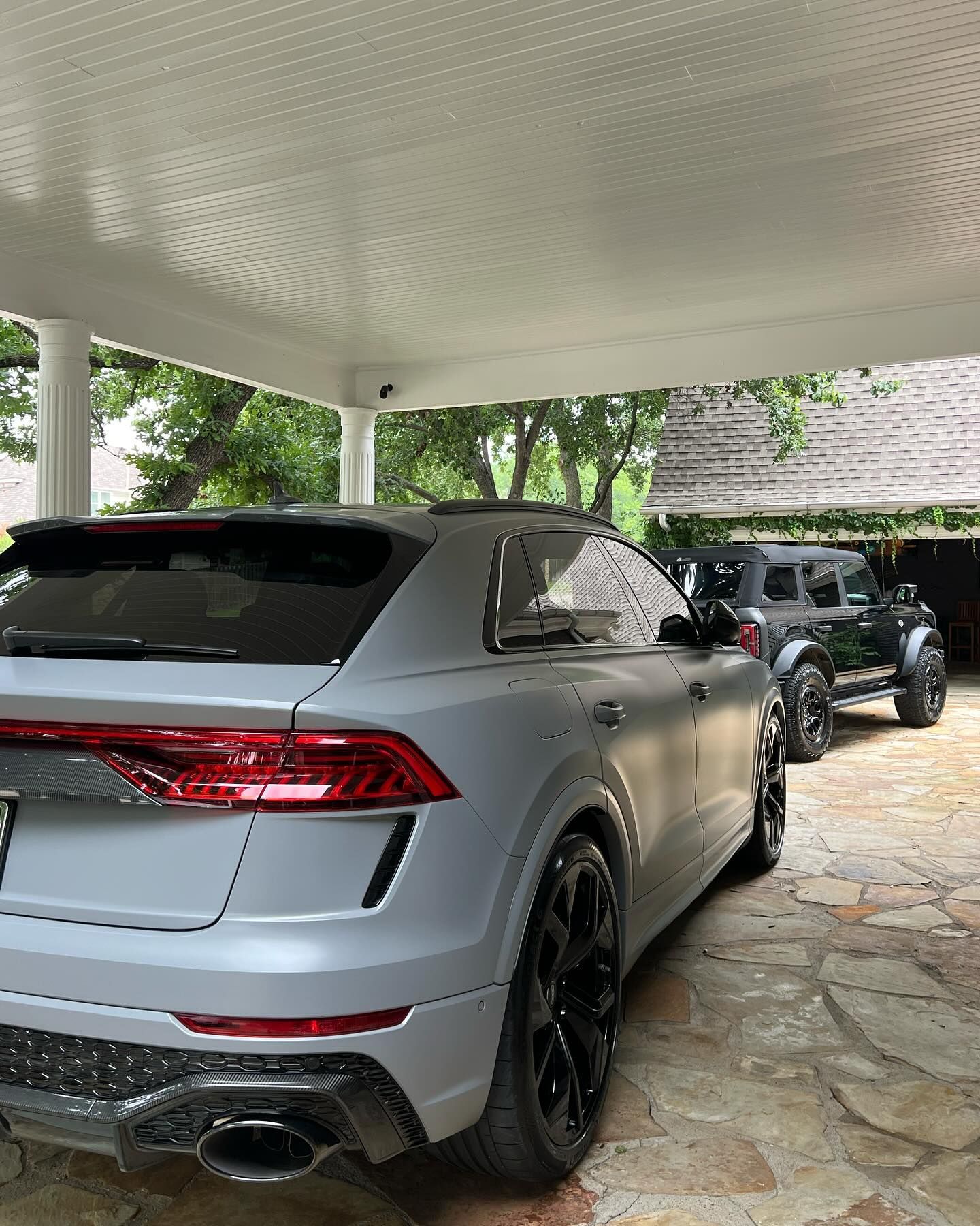 A light gray Audi SUV and black Jeep parked under a covered carport.