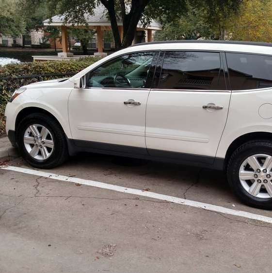 White SUV parked in a parking spot next to a curb, with trees and a building in the background.