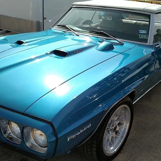 Blue 1969 Pontiac Firebird convertible with white top, hood scoops, and chrome rims.