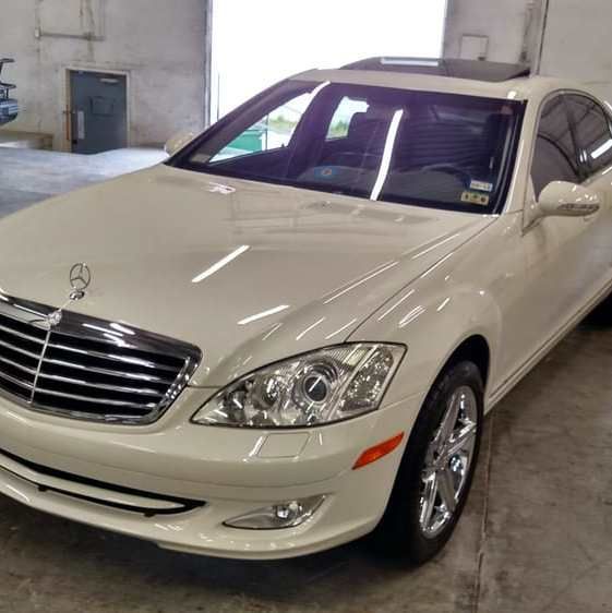 White Mercedes-Benz sedan with chrome grill and wheels, parked indoors, sunroof.