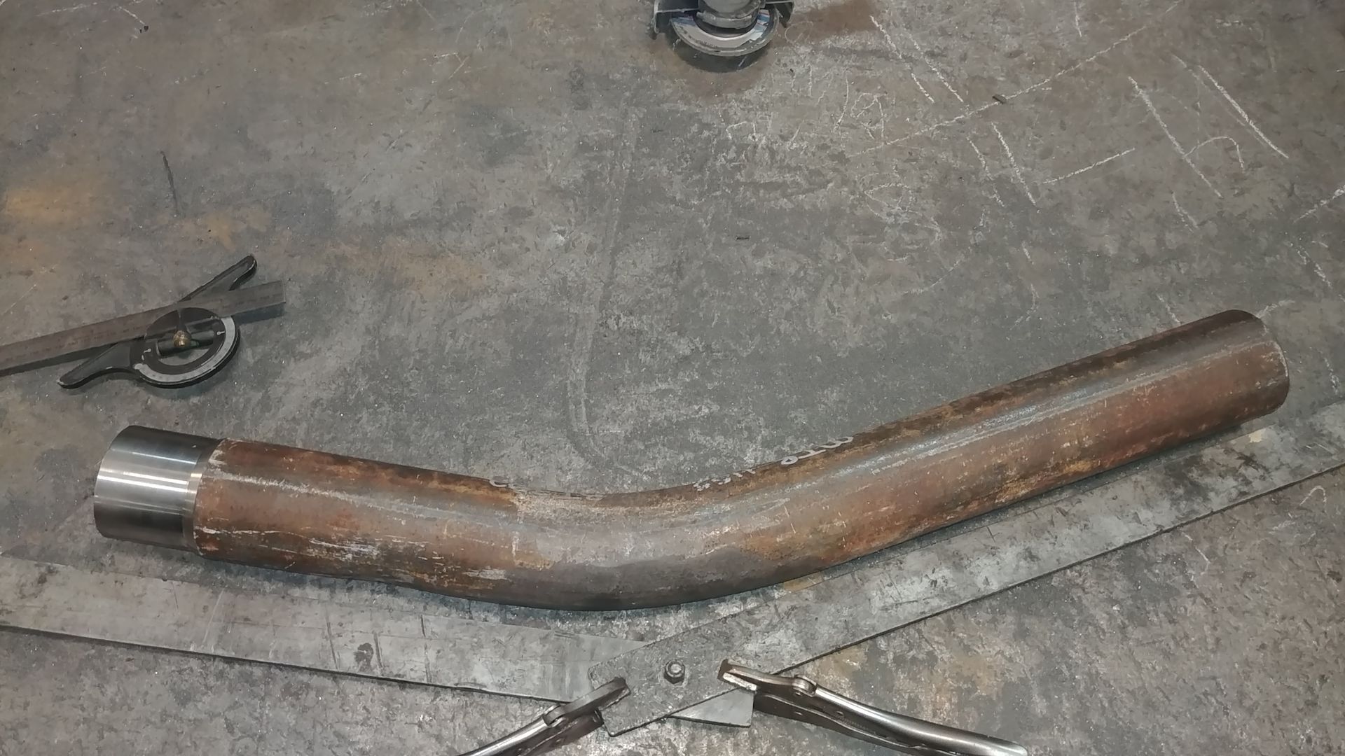 A metal pipe is sitting on a table next to a pair of pliers.