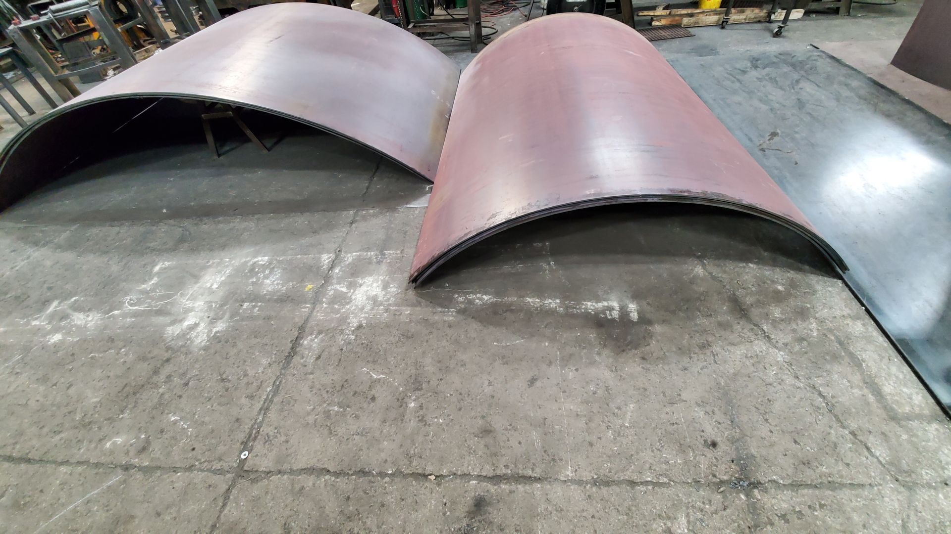 Two curved metal pieces are sitting on a tiled floor.