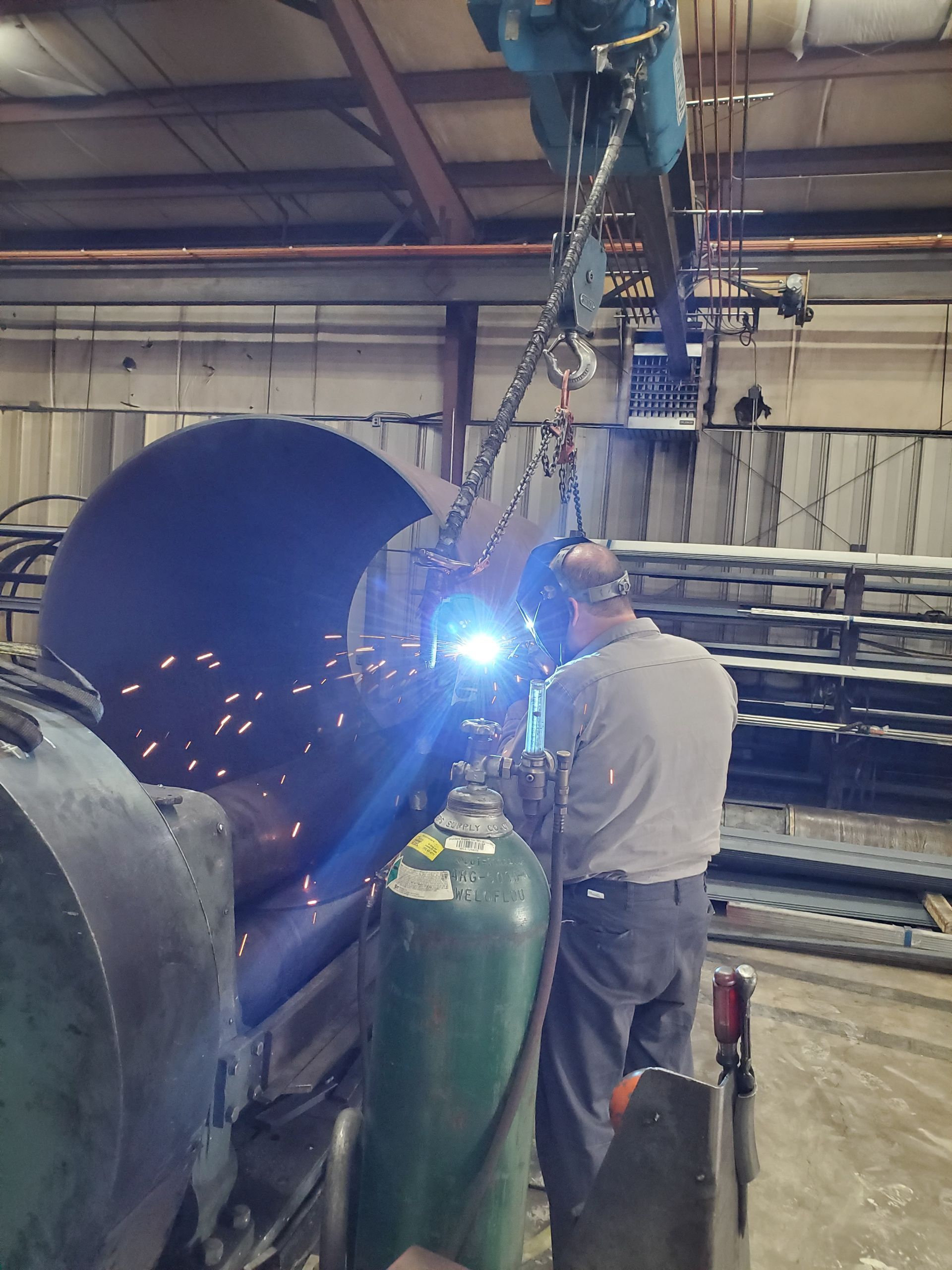 A man is welding a large pipe in a factory