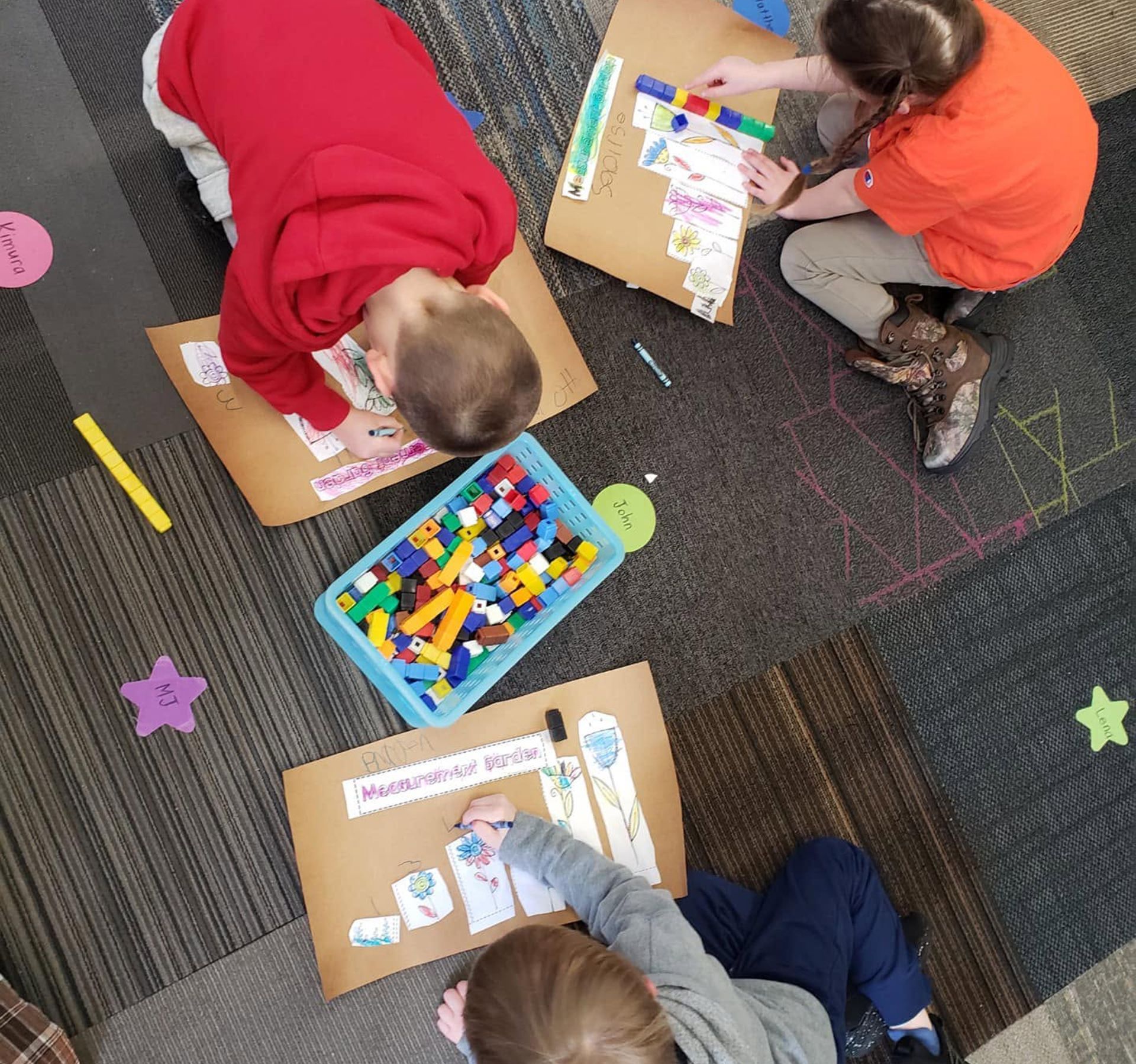 Children on carpet floor working with colorful blocks and paper labels in a classroom activity.