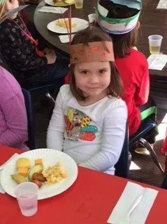 Child seated at a table with a plate of food and a drink at a school meal setting