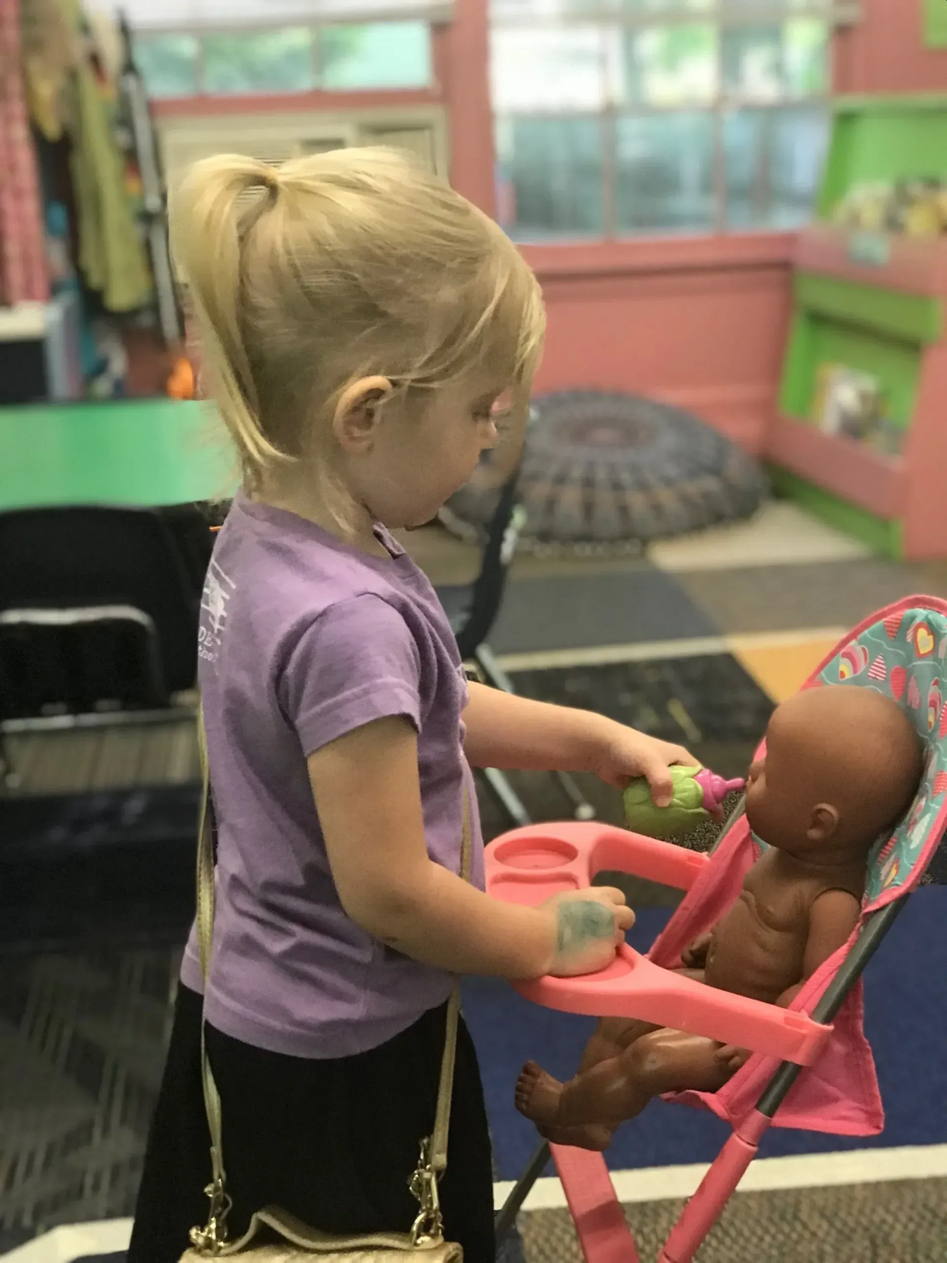 Child playing with a doll in a colorful classroom.