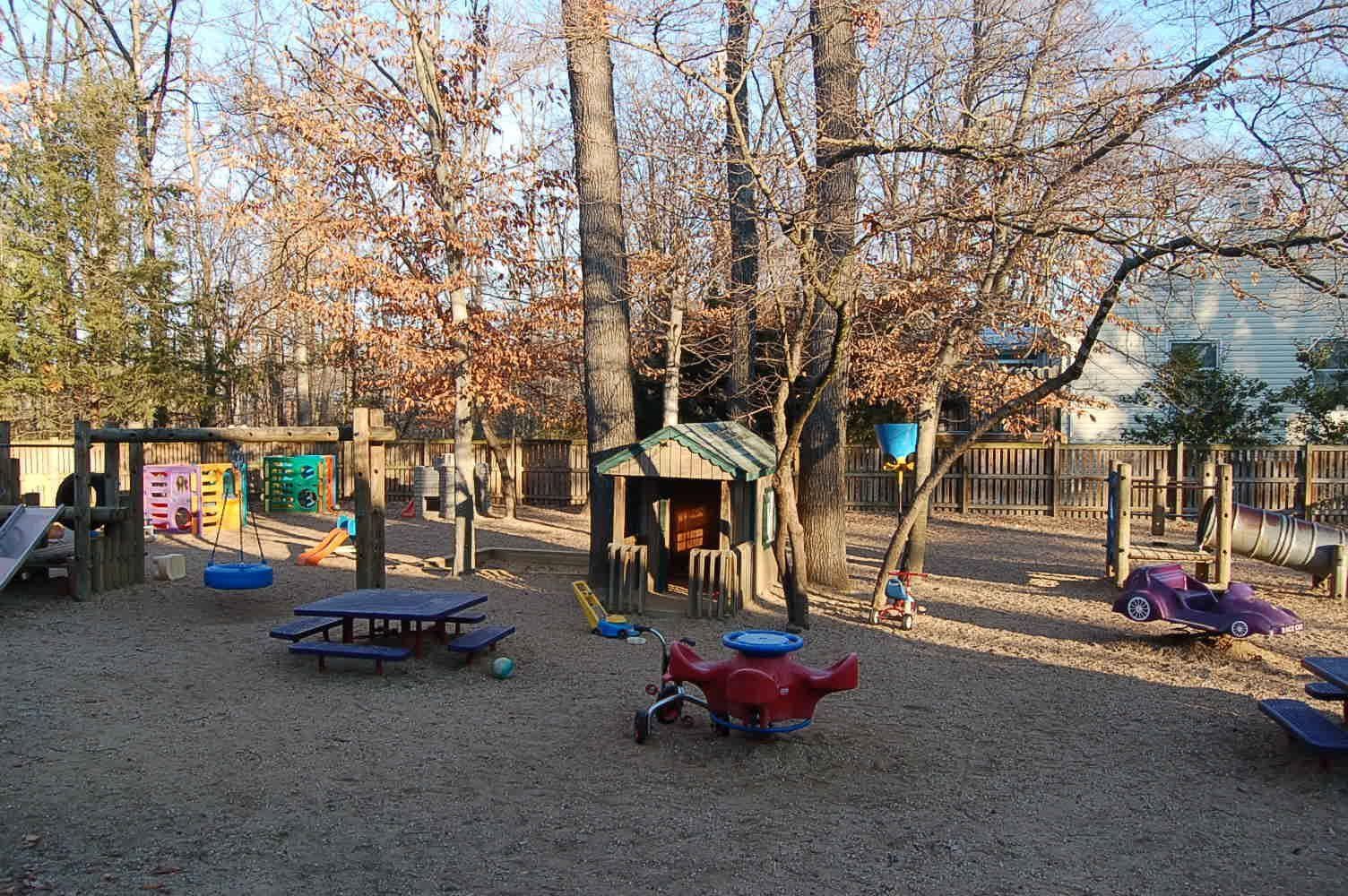 Playground with slides, climbing structures, and picnic tables among leafless trees on a sunny day