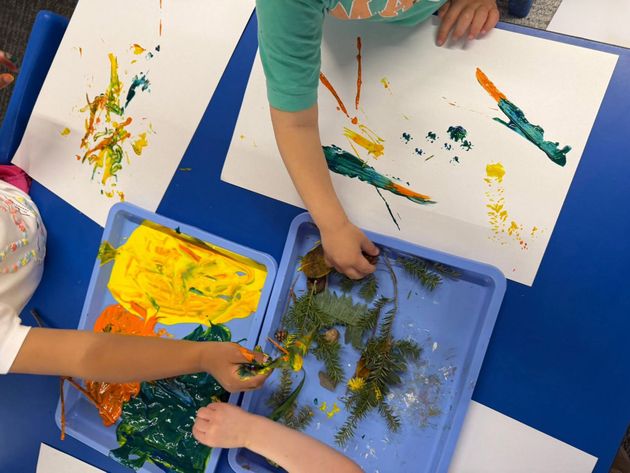 Children painting with bright colors on paper and a blue tray of paint in a classroom activity