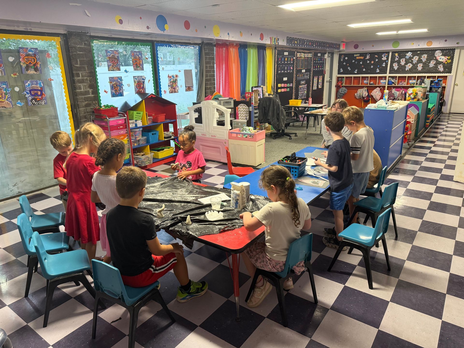 Children working at tables in a colorful classroom with checkered floor and art on the walls