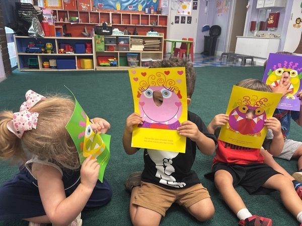 Children in a classroom hold colorful animal face art projects in front of their faces.