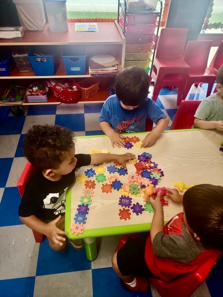 Children play with colorful shapes at a classroom table.