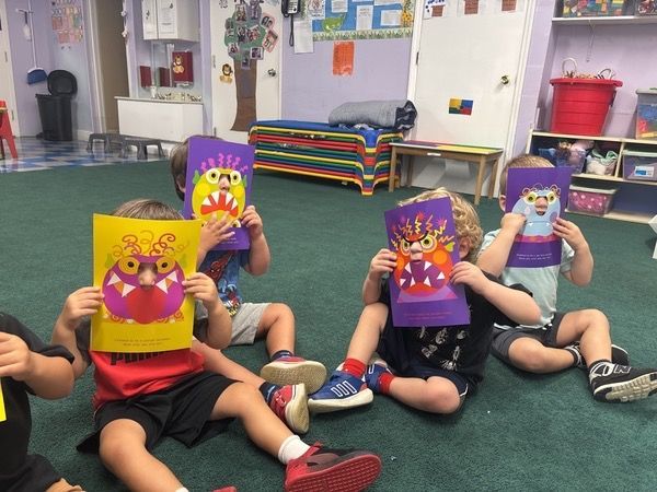 Children in a classroom sitting on the carpet, holding colorful lion masks in front of their faces.