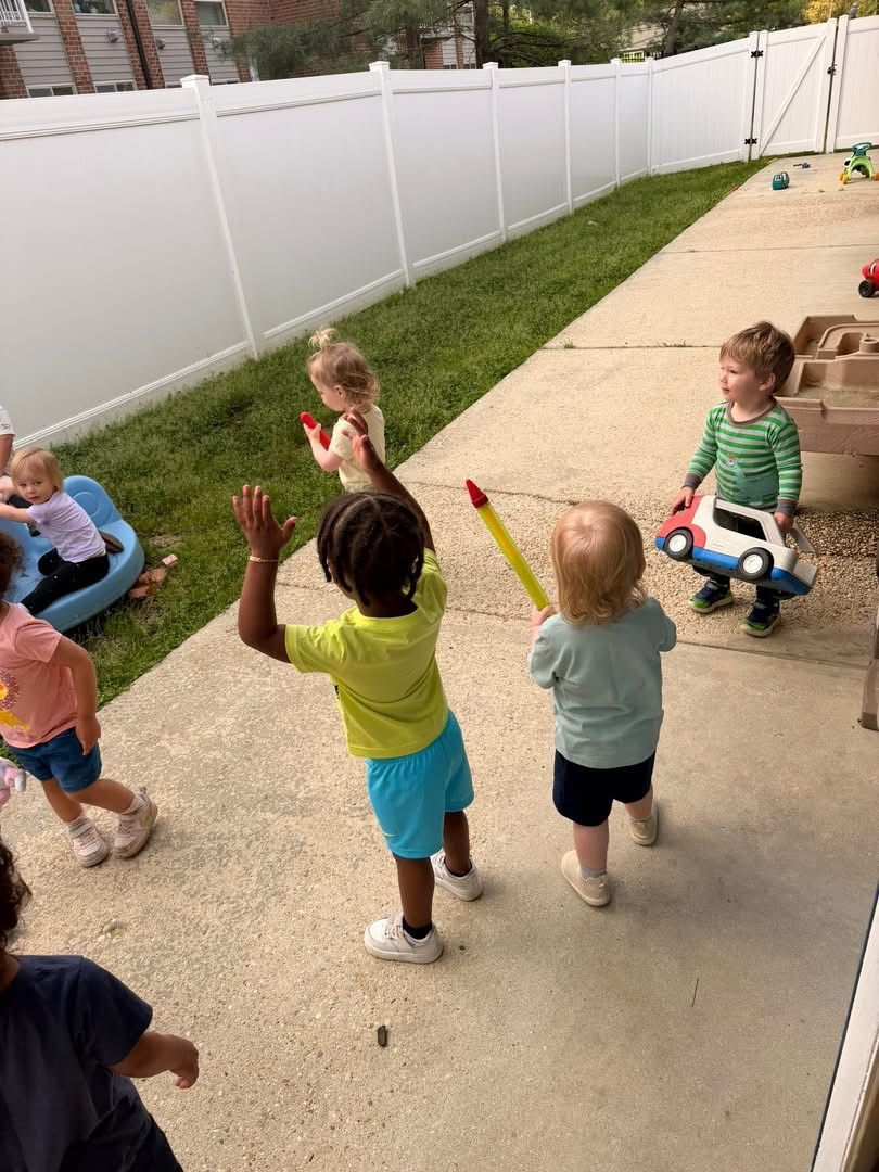 Children playing with toys in a backyard beside a white fence and patio.