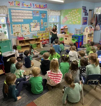 Teacher reading to seated children in a colorful classroom with wall charts and toys