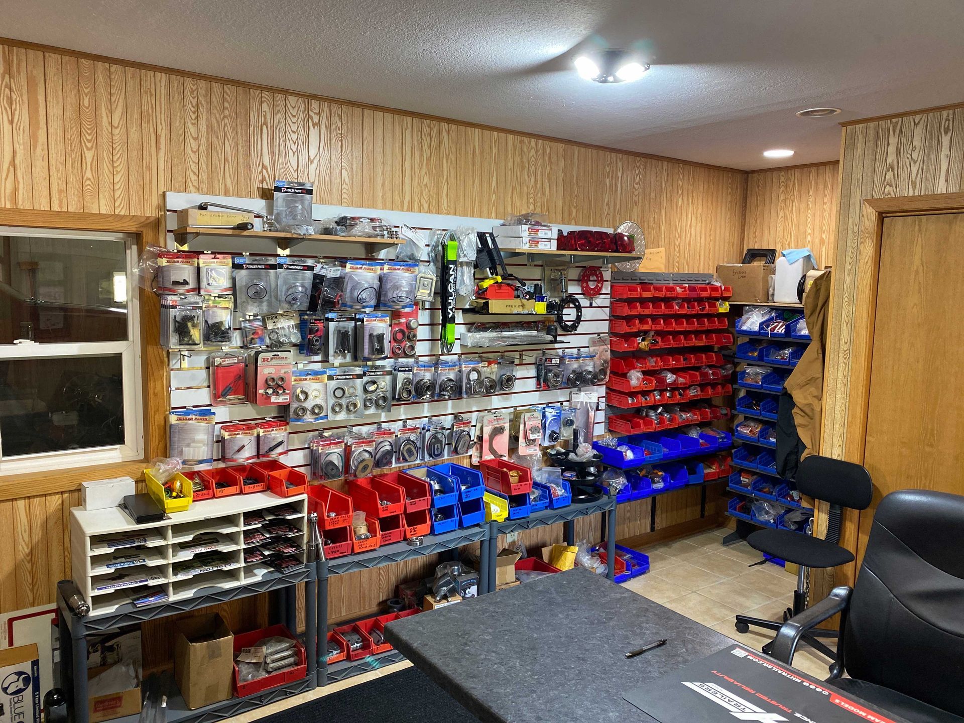 Workshop interior with parts on shelves, a desk, and a chair.