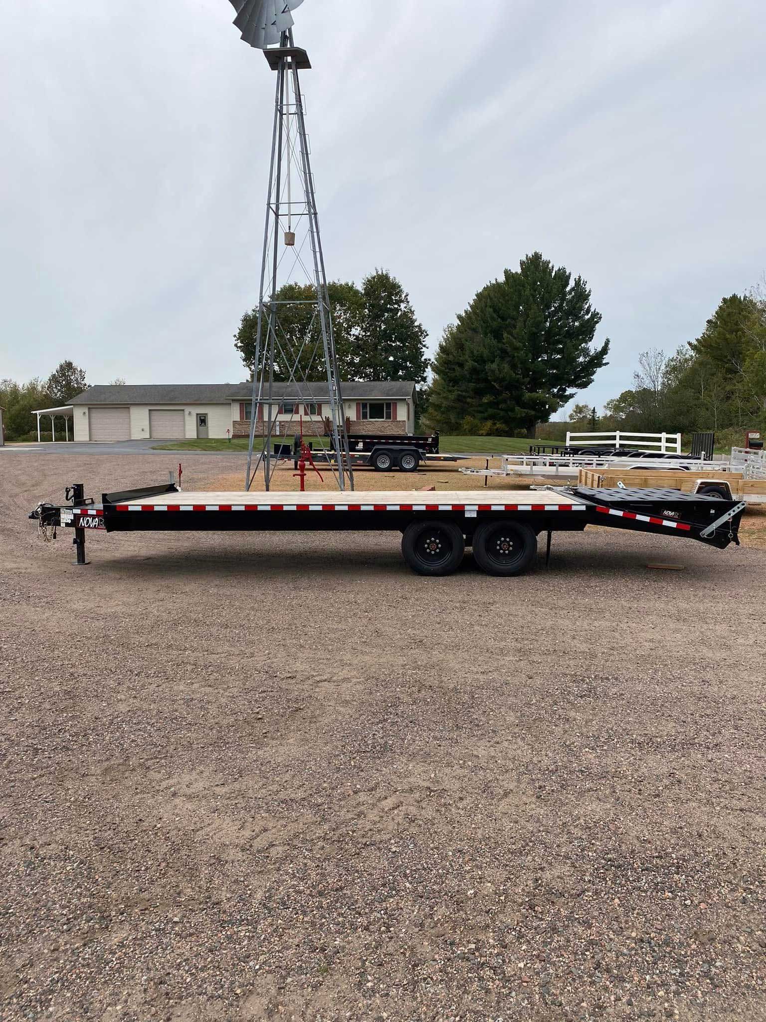 Black flatbed trailer with red and white trim, in gravel lot, windmill in background.