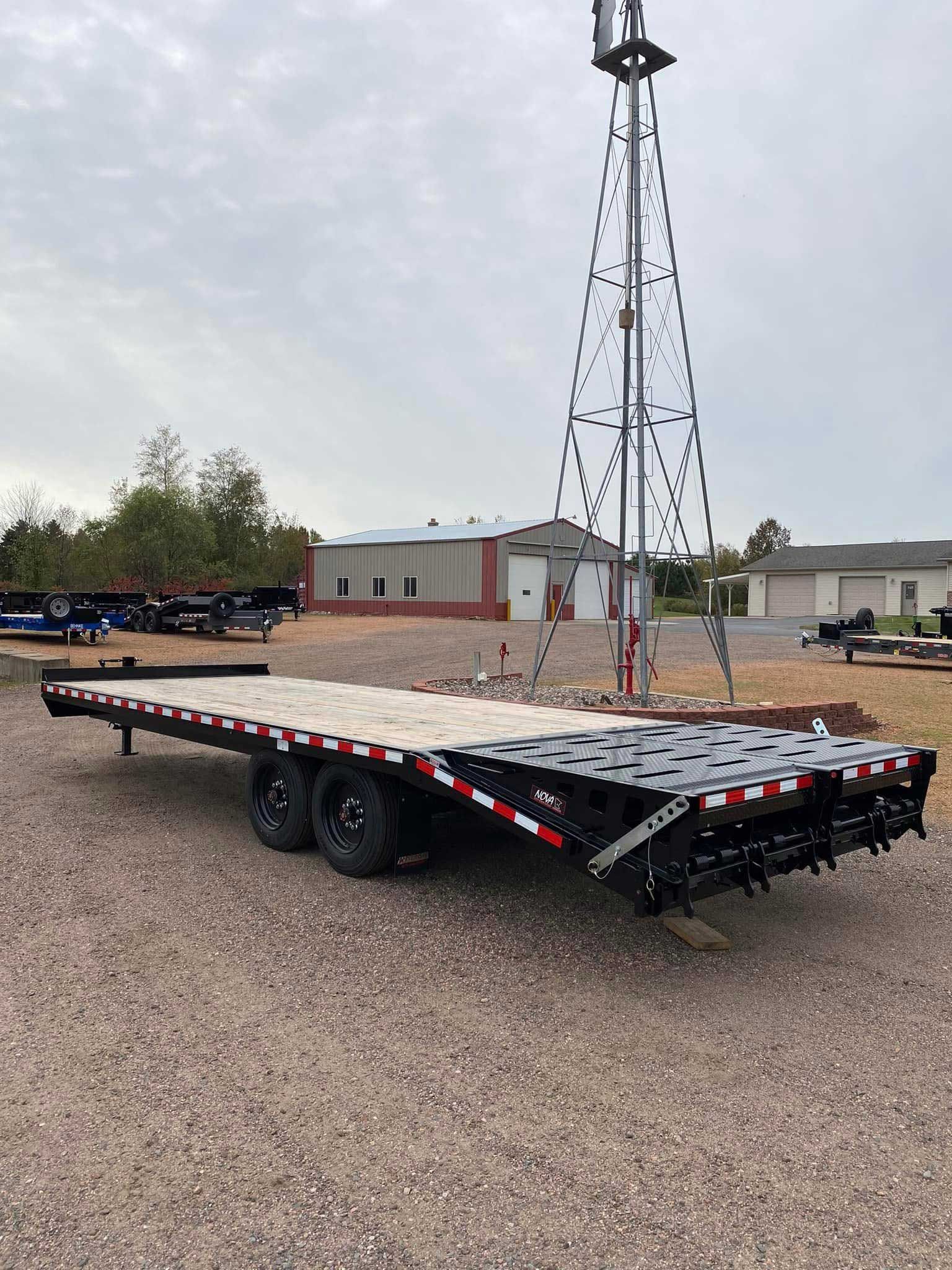 Black flatbed trailer with wooden deck, near a windmill and a building.