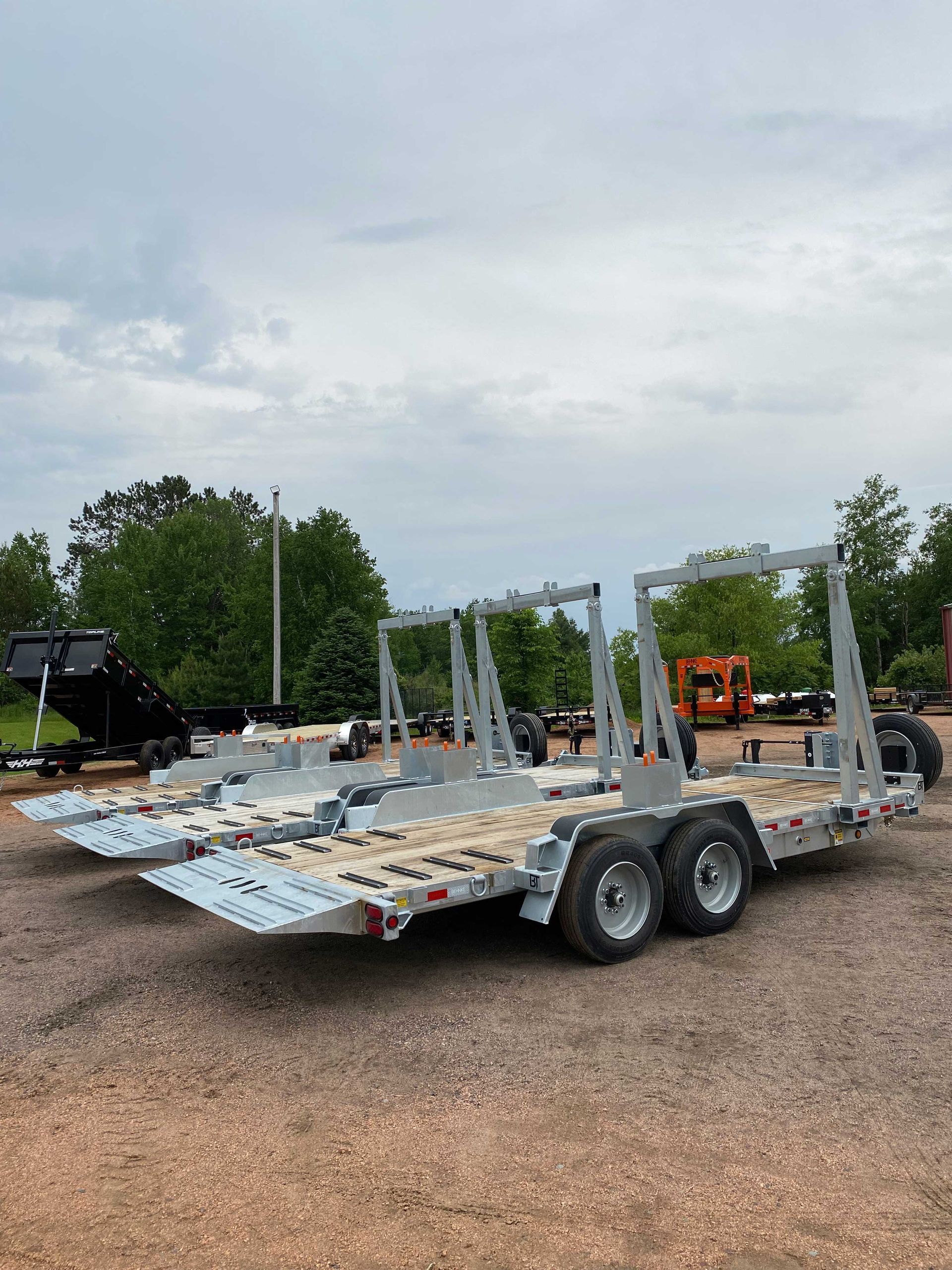 Two gray trailers with side rails, parked outdoors on gravel.