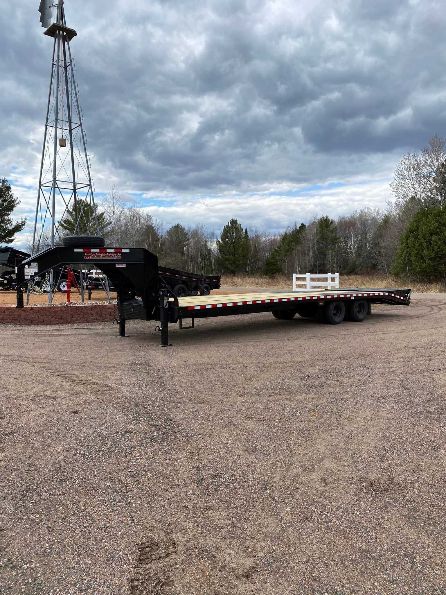 Black trailer parked outdoors near a windmill under a cloudy sky.