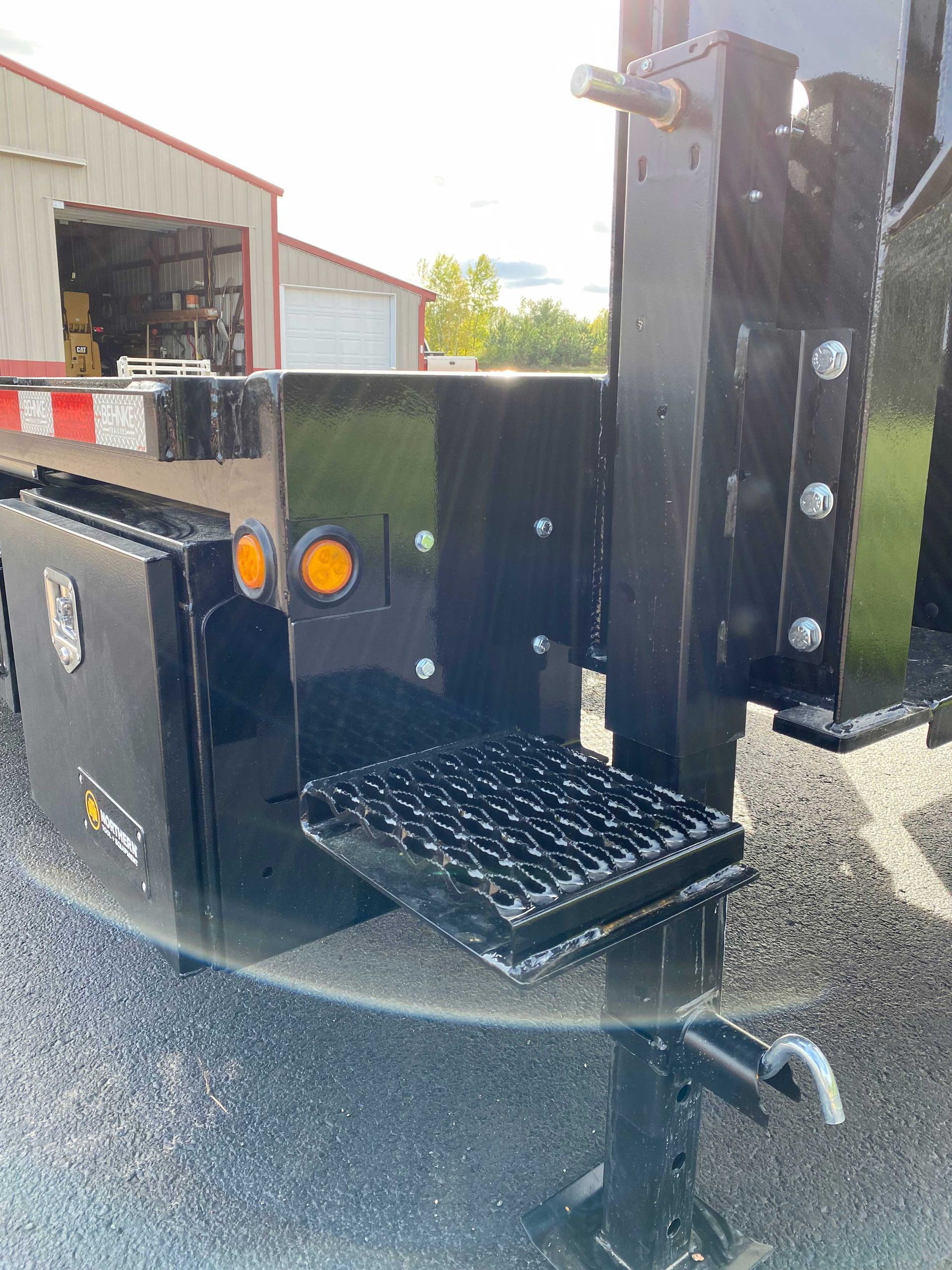 Black trailer front with step, amber lights, and bolted construction. Outdoors.