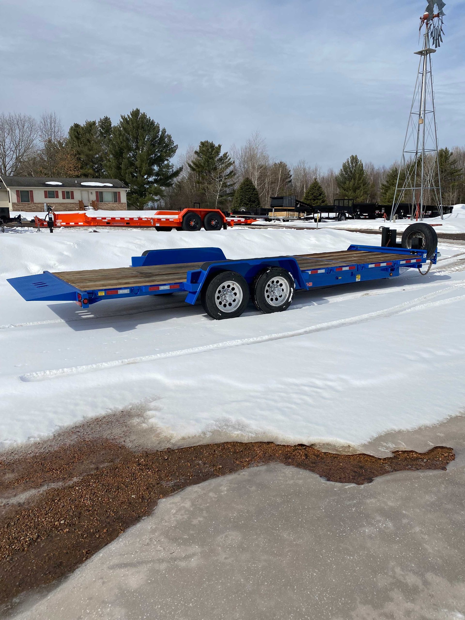 Blue trailer on snowy ground. Additional trailers and tower in the background.