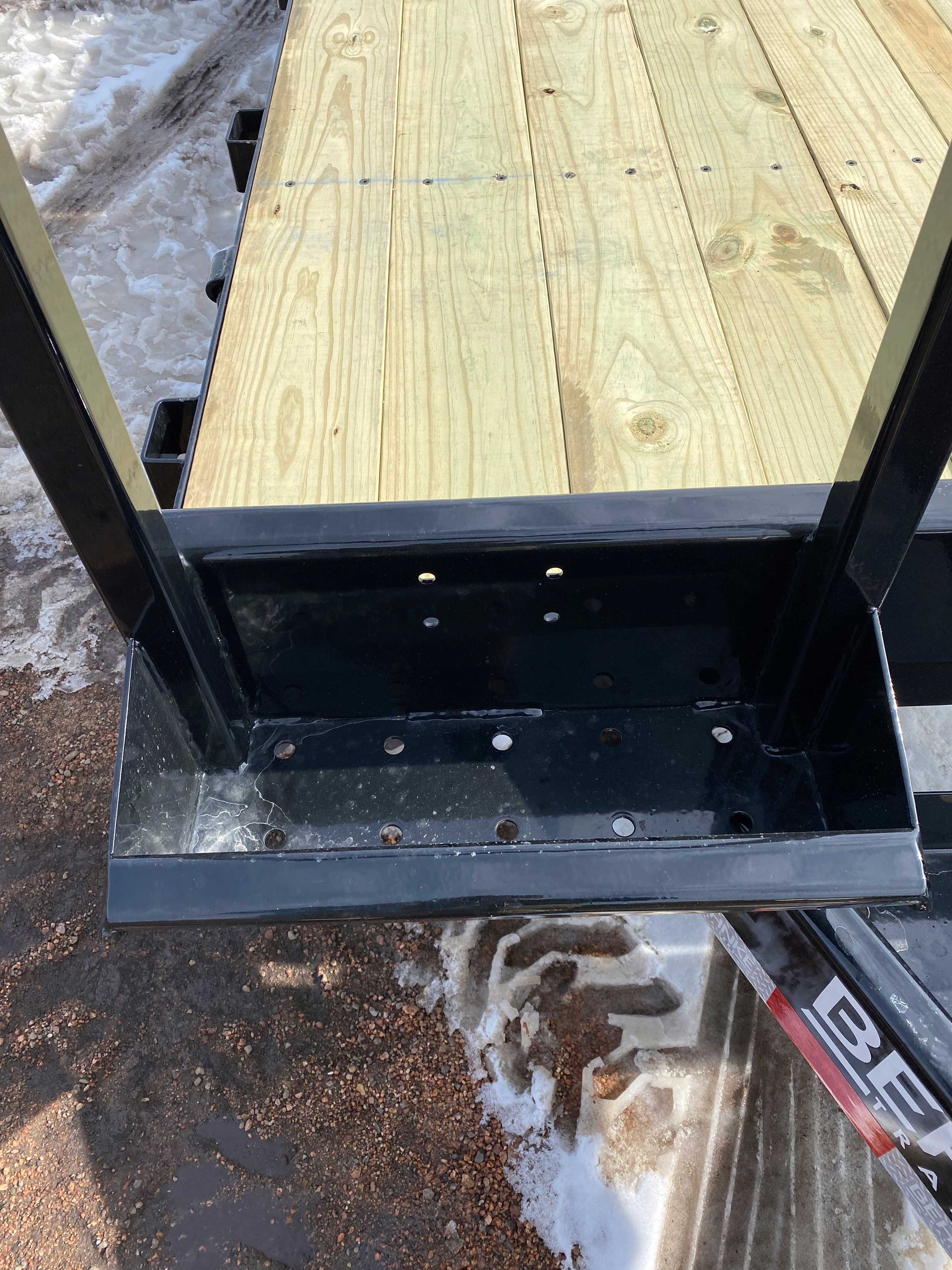 Black metal box with support posts bolted to a wooden deck, covered with light-colored boards.