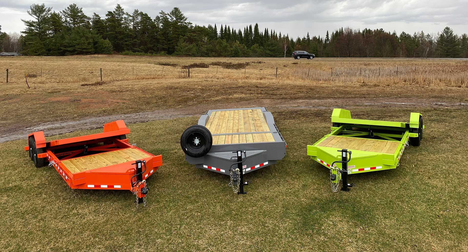 Three colorful flatbed trailers parked on a grassy field with a road in the background.