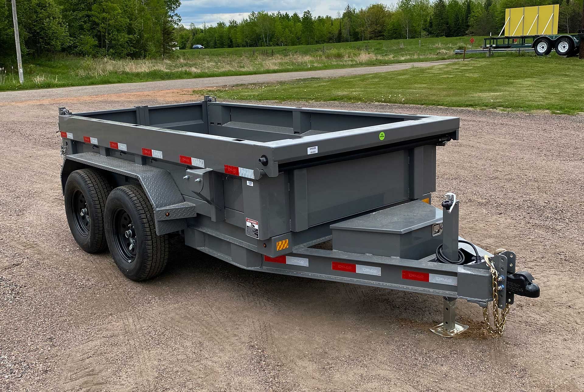 Gray dump trailer on gravel in a field with other trailers in the background.