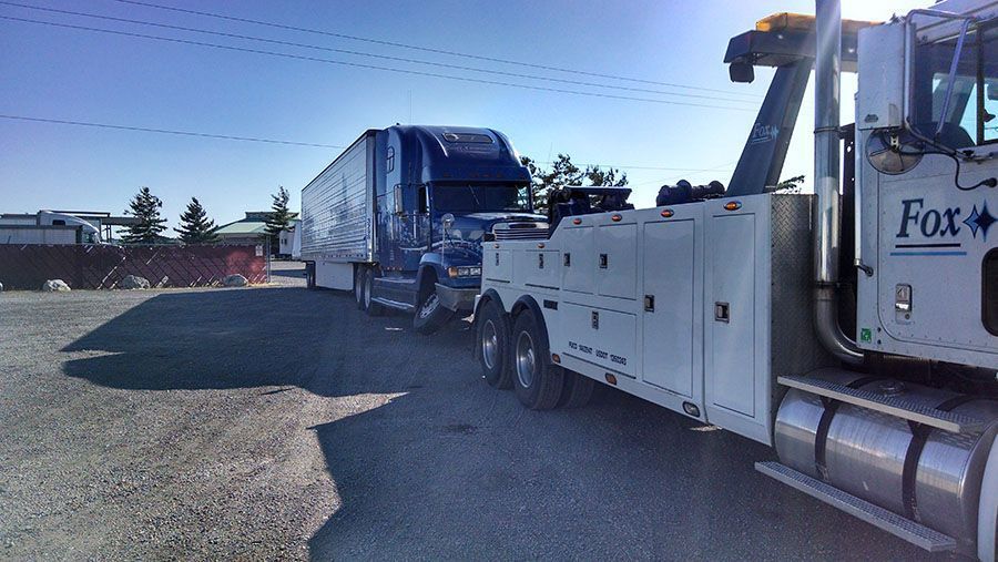 Tow truck towing a semi-truck in a sunny parking lot. 