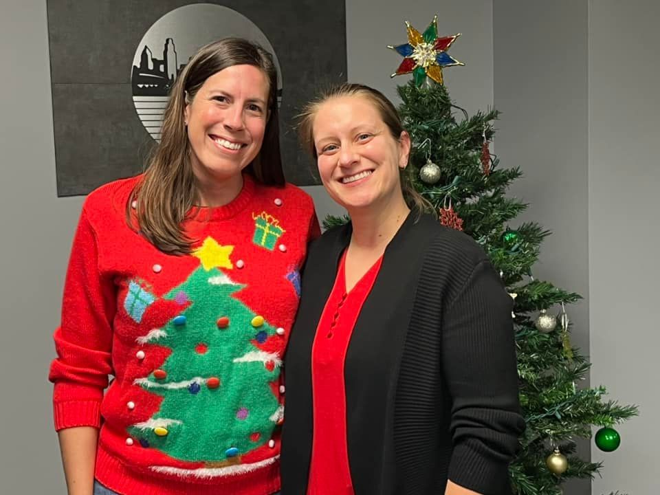 Two women are posing for a picture in front of a christmas tree.