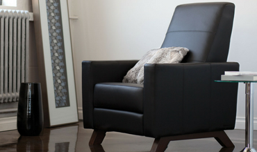 A black leather chair is in a living room next to a table