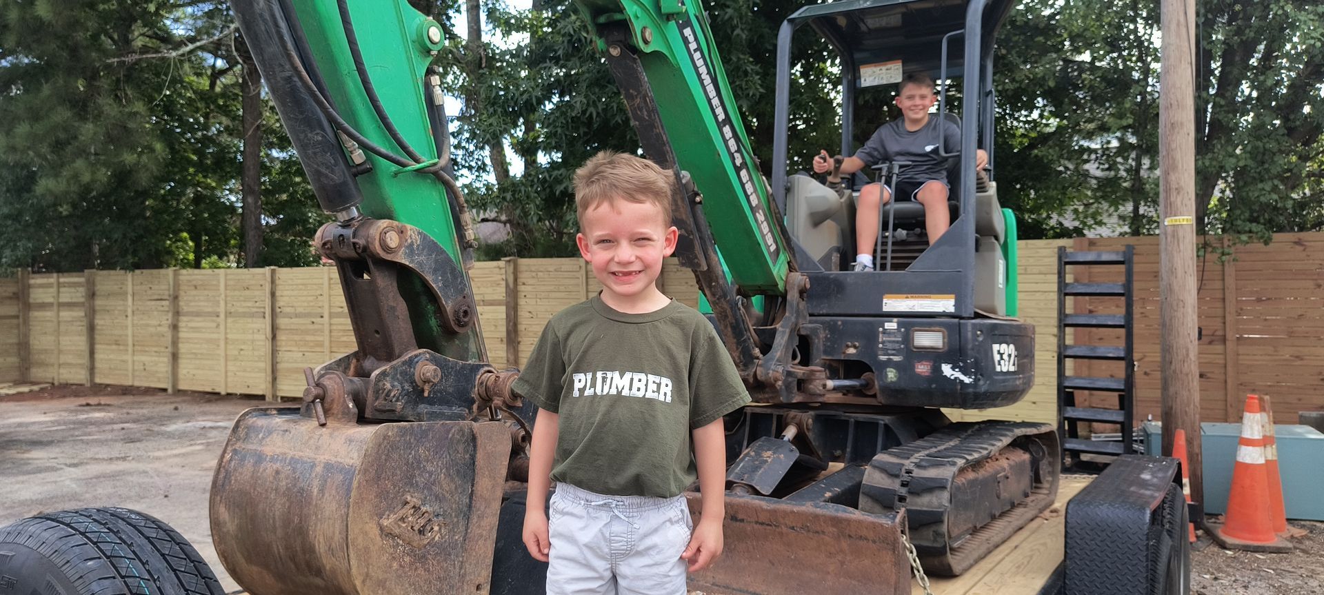 A young boy is standing in front of a green excavator.