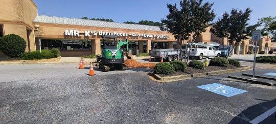 A green excavator is sitting in a parking lot in front of a building.