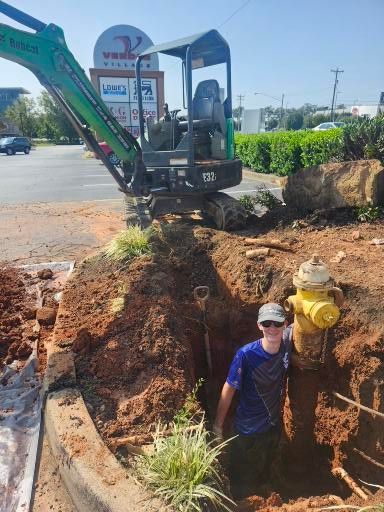 A man is standing in a hole next to a fire hydrant.