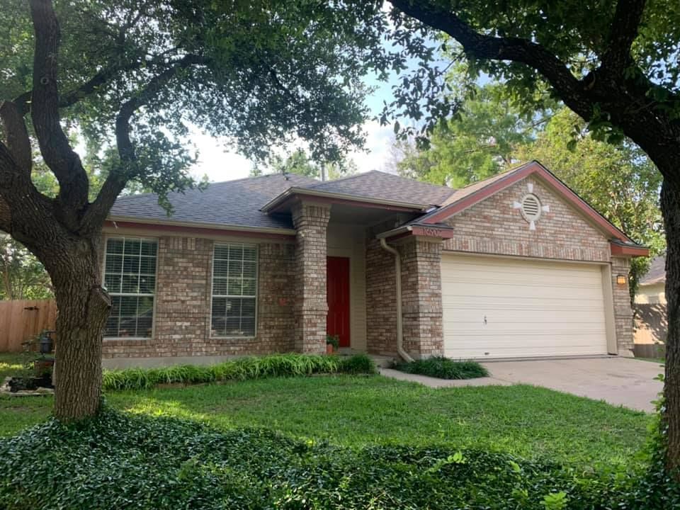 A brick house with a white garage door and a tree in front of it.