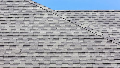 A close up of a gray shingle roof with a blue sky in the background.