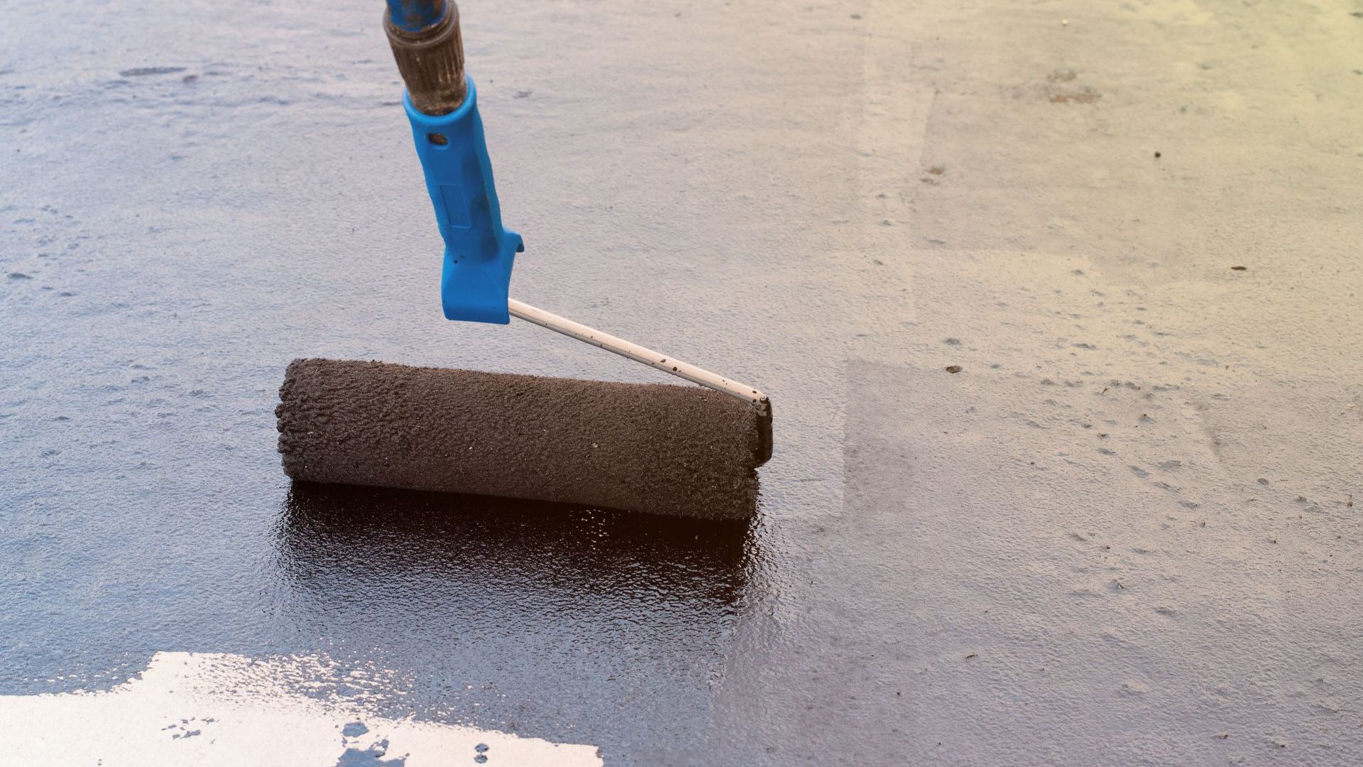 A person is painting a concrete floor with a roller.