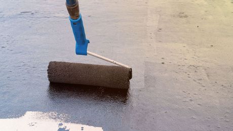 A person is painting a concrete floor with a roller.
