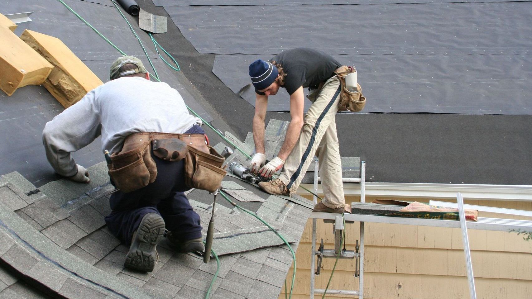 Two men are working on the roof of a house.