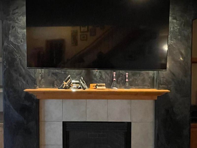 Fireplace with mounted TV, gray tile, wooden mantel, and dark gray wall accent.