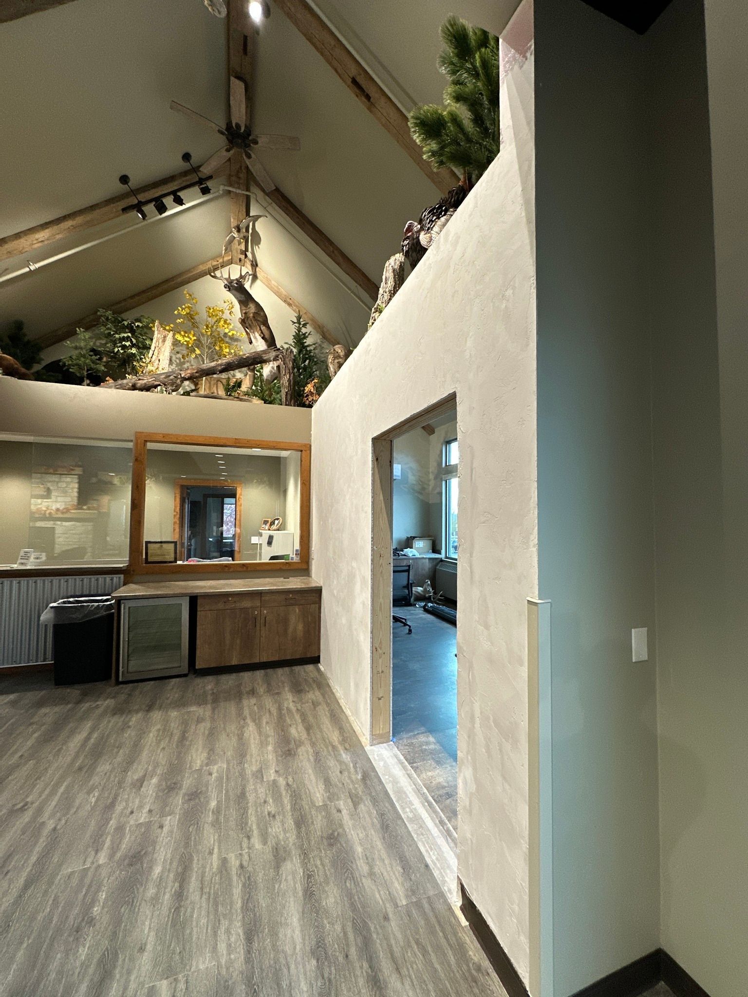 Interior office space with doorway, mirror, wood cabinets, and artificial plants.