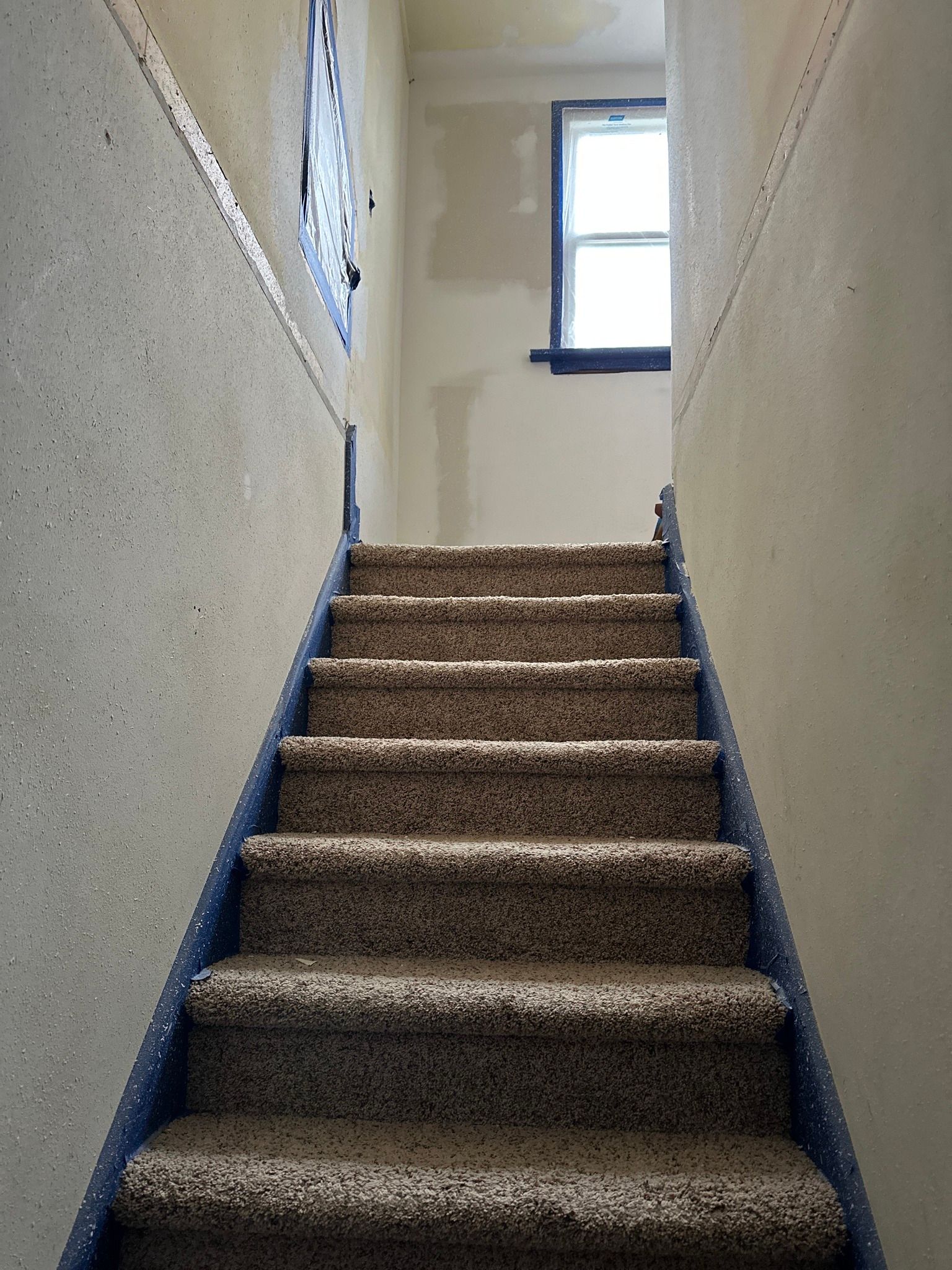 Staircase with carpeted steps and textured walls, leading towards a window at the top.