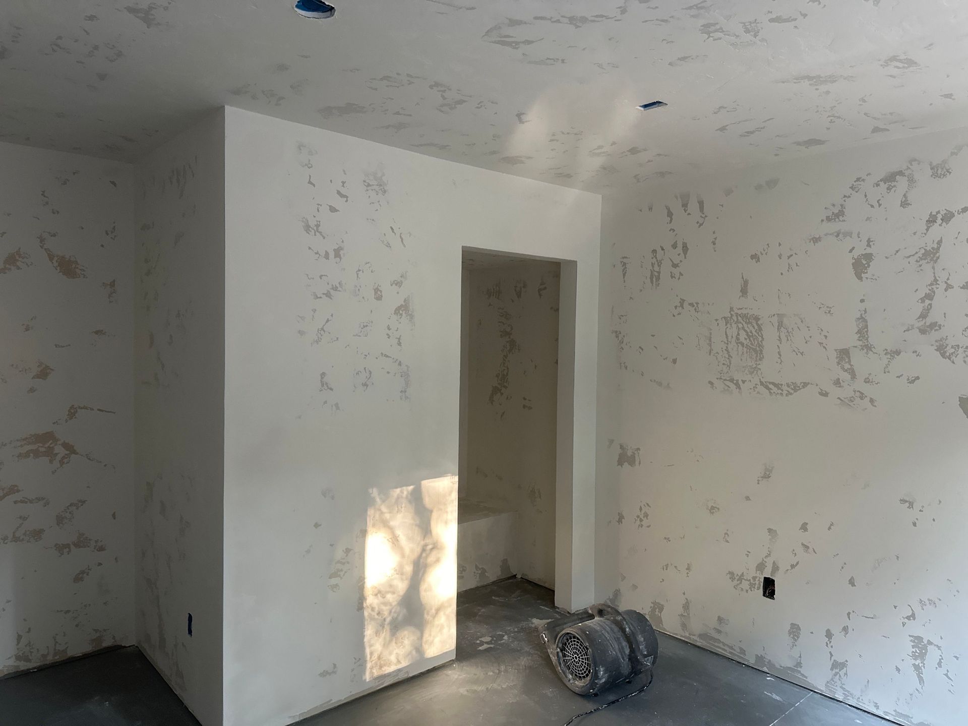 Empty room with textured, light-colored walls, doorway, and concrete floor; construction in progress.