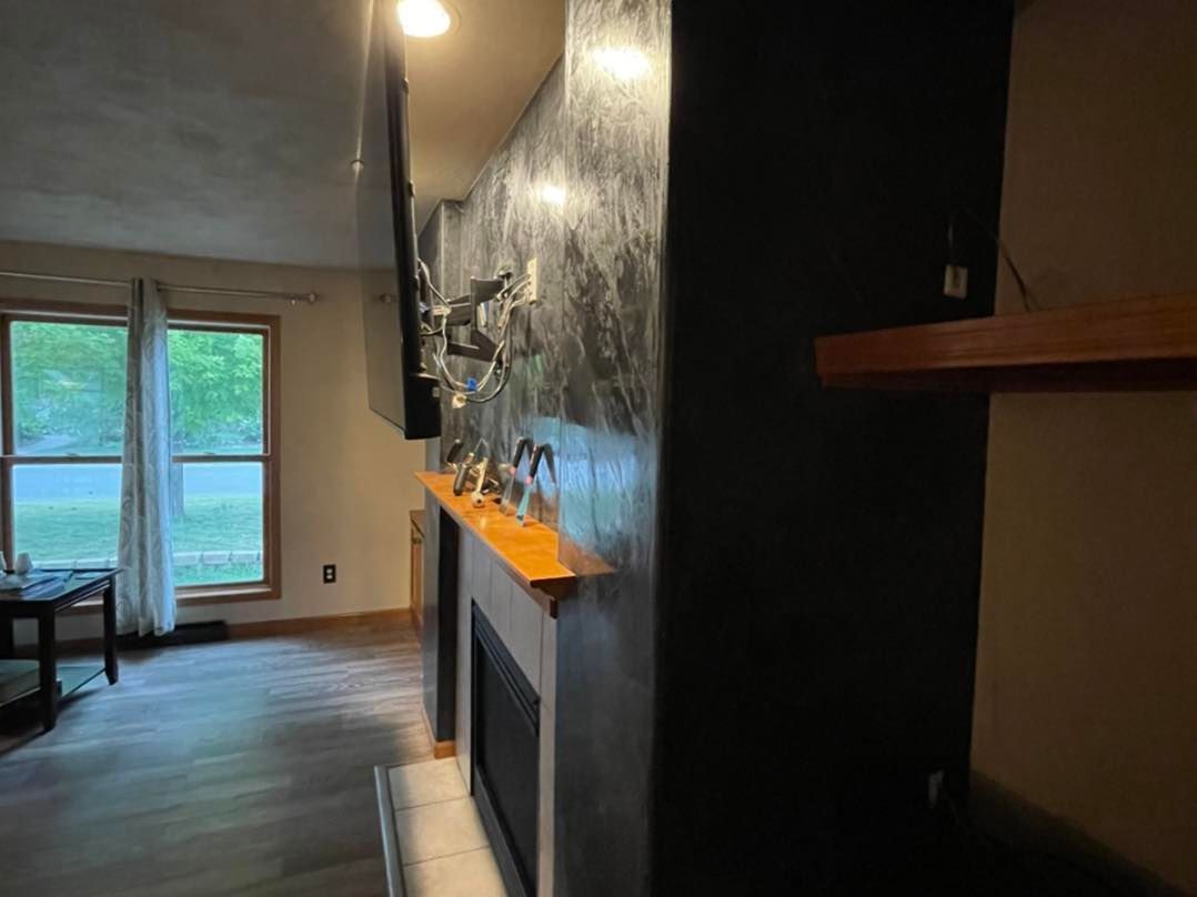 Living room with fireplace, TV, windows, and wood floor. Black accent wall with metallic finish.