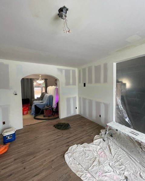 Room under construction; drywall installed, unfinished ceiling, plastic covering furniture.