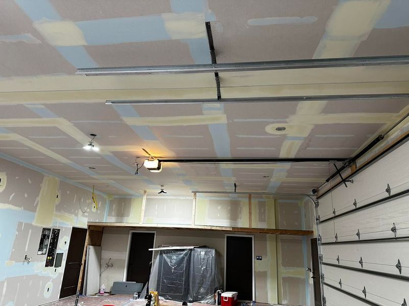 Interior of a garage under construction with drywall and ceiling tracks visible.