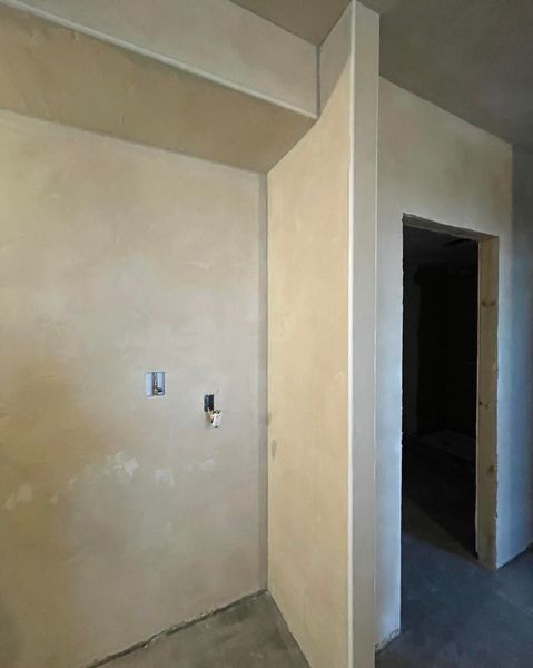 Beige walls in a room under construction, with an open doorway to another room.